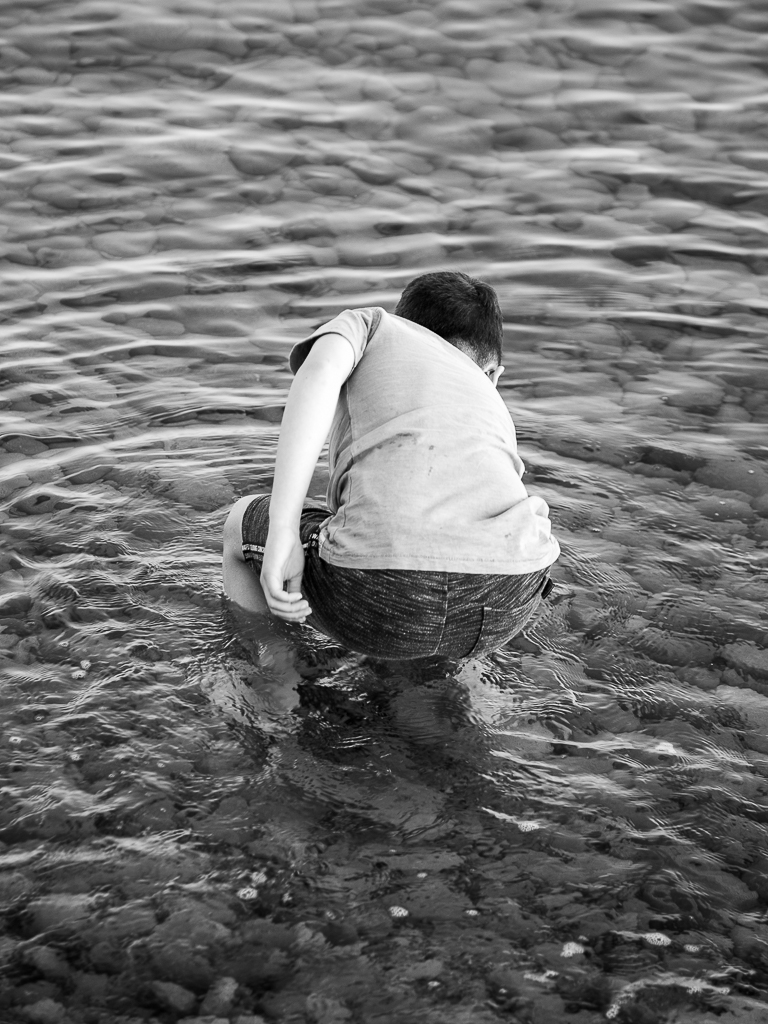 Jongen pakt een pebblestone uit het water